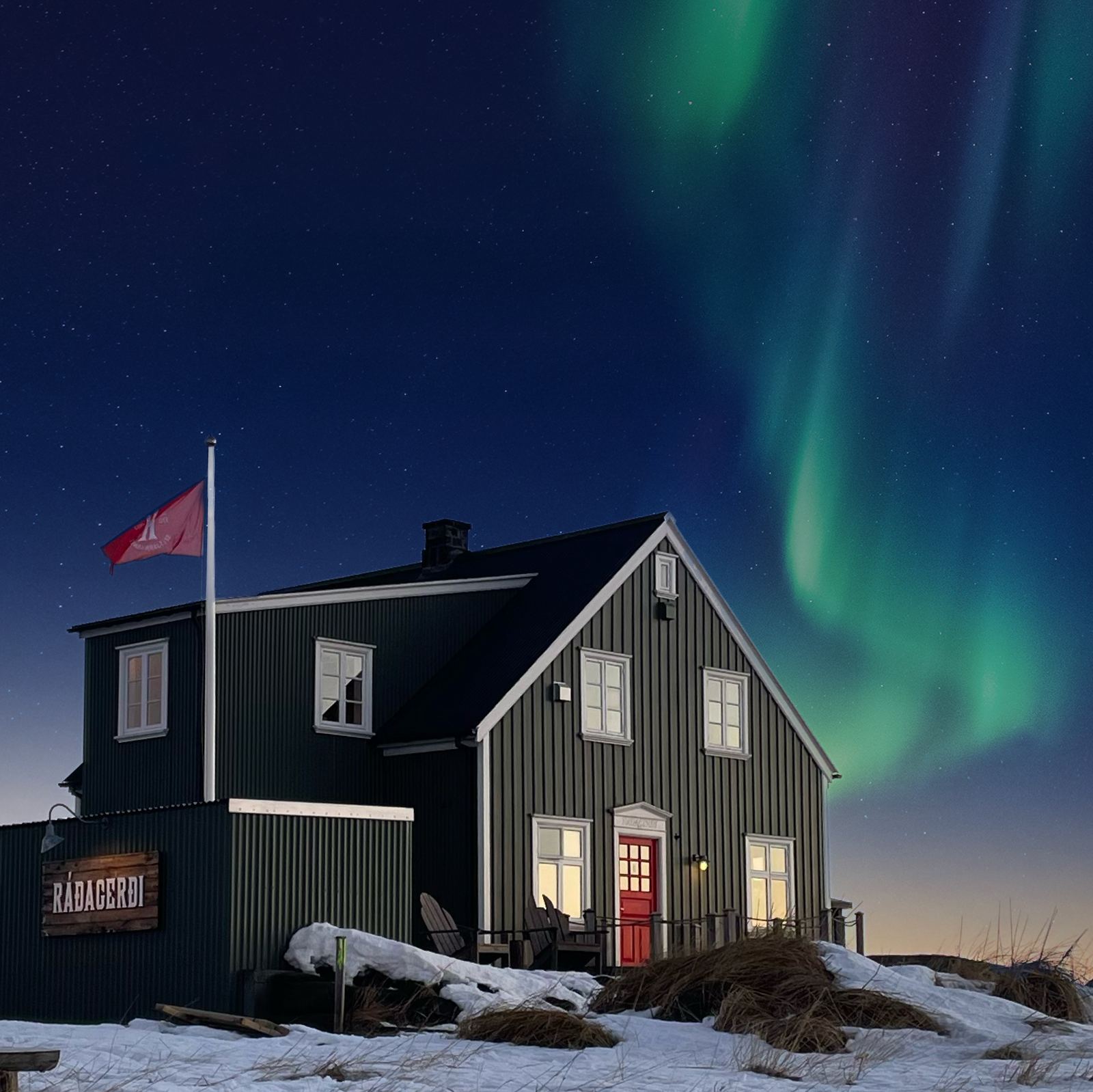 Ráðagerði að kvöldi til í snjó, ljós í gluggum og norðurljós á himni